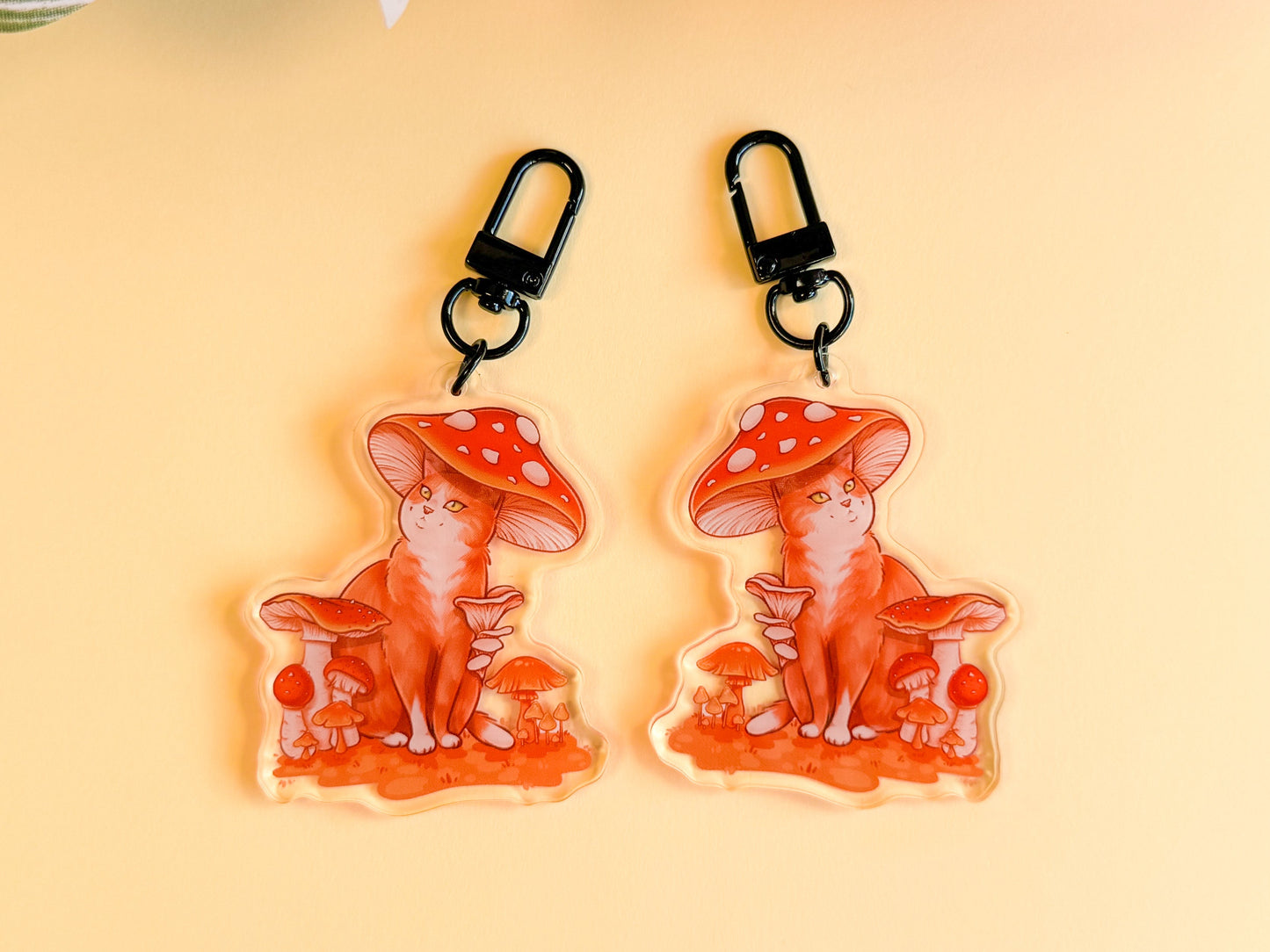 Two keychains of cats with red mushroom hats on a yellow background