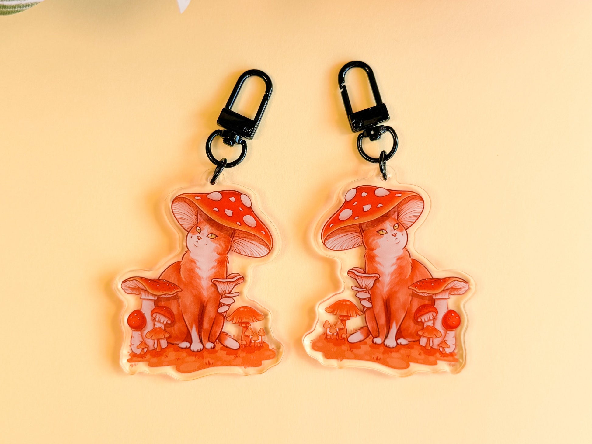 Two keychains of cats with red mushroom hats on a yellow background